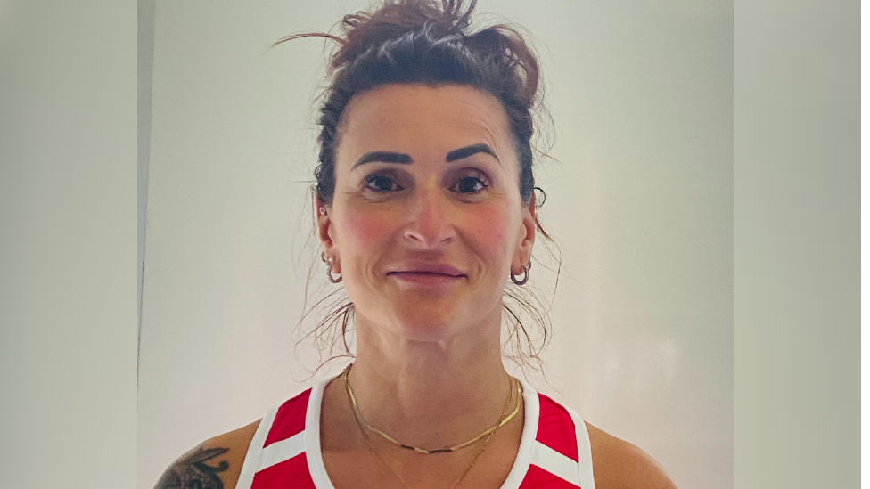 Sabina Falcone-Healey. She has dark hair, which is tied up in a bun. She is wearing a red and white vest. She is pictured against a plain background and is looking directly at the camera and smiling.