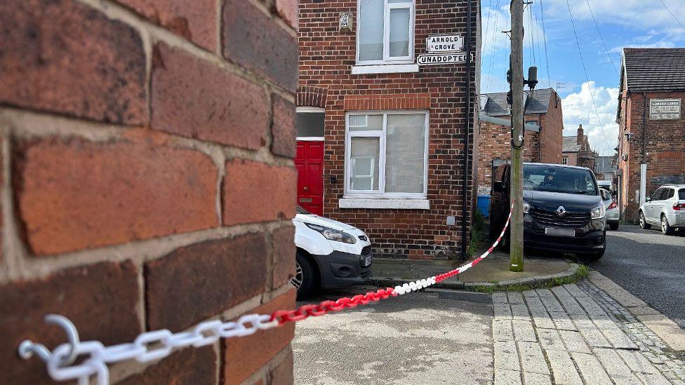 The end of a terraced street with a red and white plastic chain hung across the road attached to a wall and a lampost