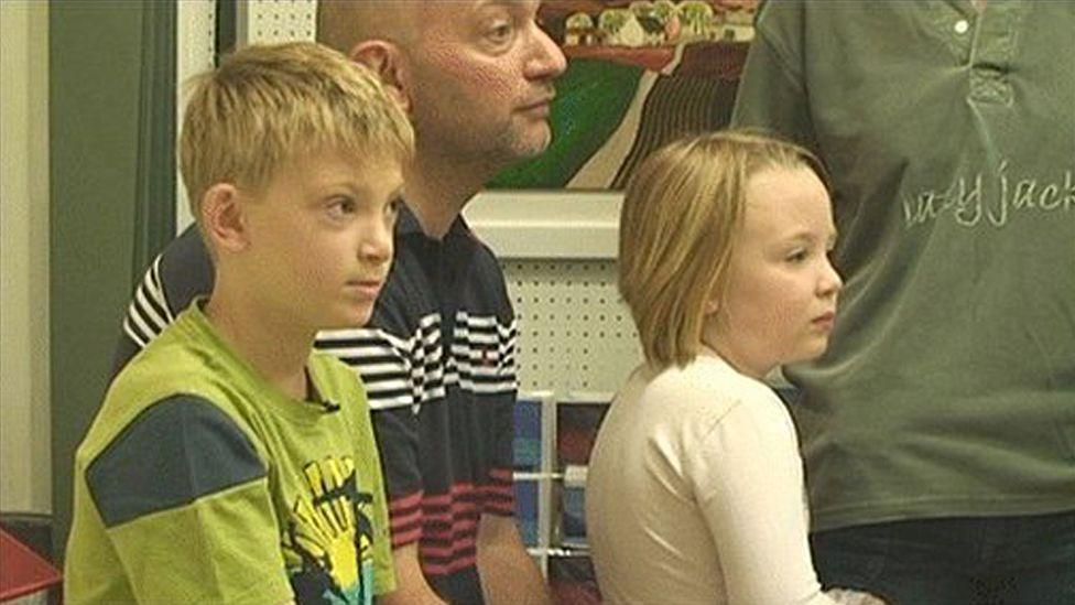 Kieron, Keith and Billie-Jo Williamson sat in a gallery, looking into the space where Kieron's work is being auctioned (out of picture). Kieron is wearing a green T-shirt. His father has a striped polo-neck shirt and his sister has a white top.