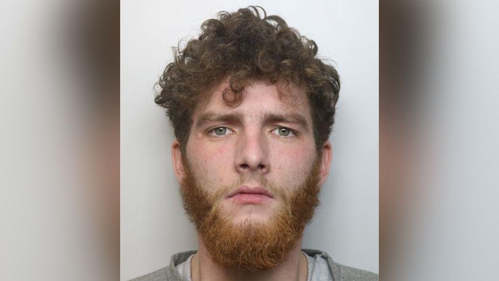 A police mugshot of Joshua Coulton, who has curly red hair and a thick beard.