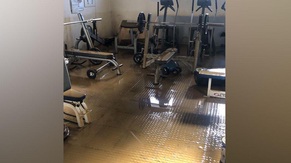 Gym equipment in a room covered with dirty brown water.