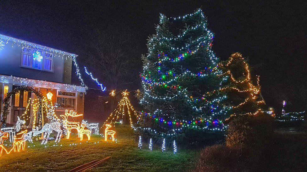 Ms Bretton's house bedecked in Christmas lights. Lights cover the house and the garden. Lights have also been draped around a large tree. 