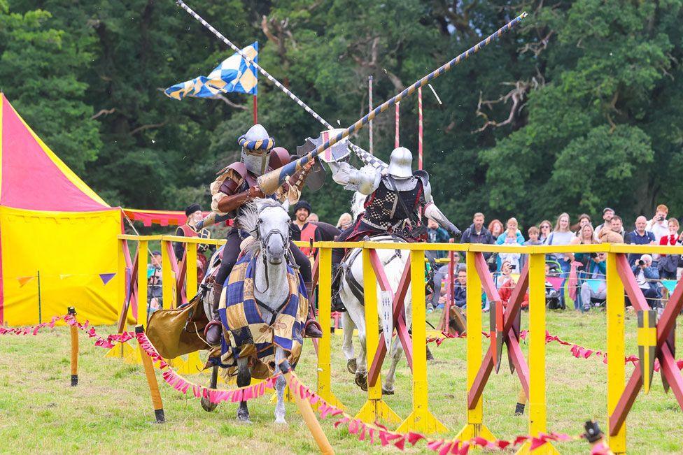 Two knights on horseback recreate a historic joust with lances high in the air and big crowds looking on