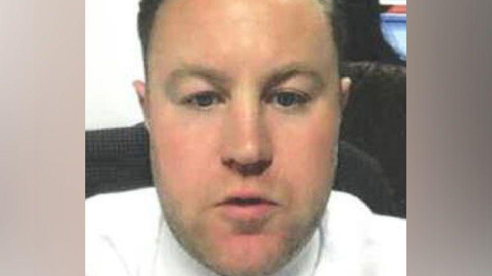 A head image of Benjamin Cazaly - he has short brown hair and stubble, is wearing a white shirt.
