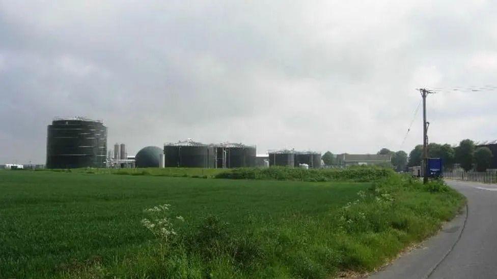 An anaerobic digester plant. It consists of five dark green, round buildings