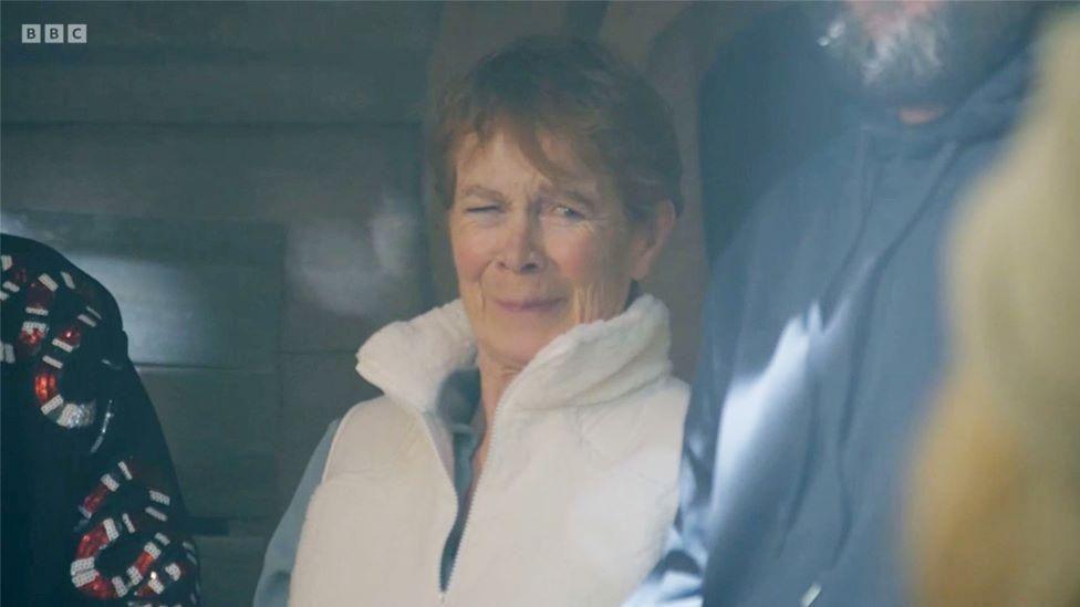 An image of Celia Imrie in the Celebrity Traitors after she farted in episode three. Celia has one eye closed and is wearing an amused facial expression. She is wearing a white gilet and blue shirt.