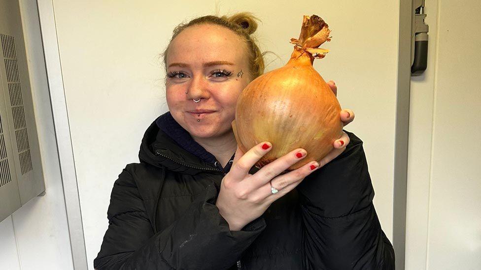 A white woman with red nails holding a Spanish onion the size of her head