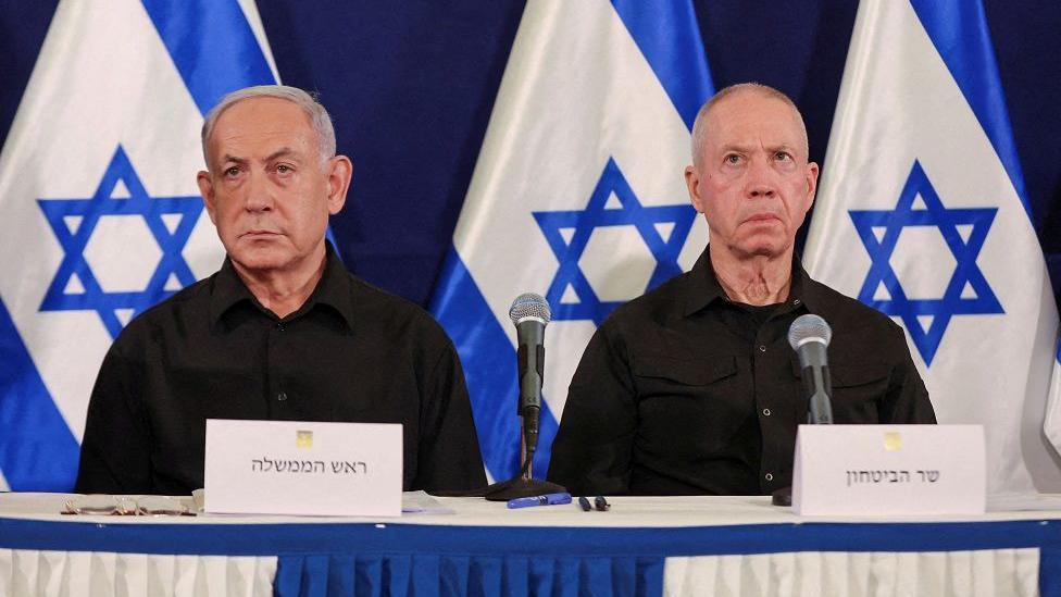 Benjamin Netanyahu sits next to Yoav Gallant during a press conference, with the Israeli flag behind them