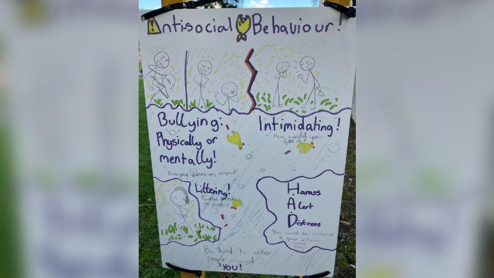 A close up photo of Mia's sign which says 'anti-social behaviour' at the top with stick figures demonstrating anger with words such as 'bullying, physically or mentally', 'intimidating' and 'harass, alert, distress'.