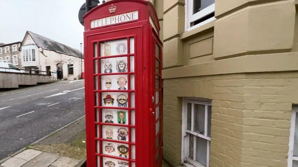 Red telephone box with cartoon drawings of people stuck in the windows.