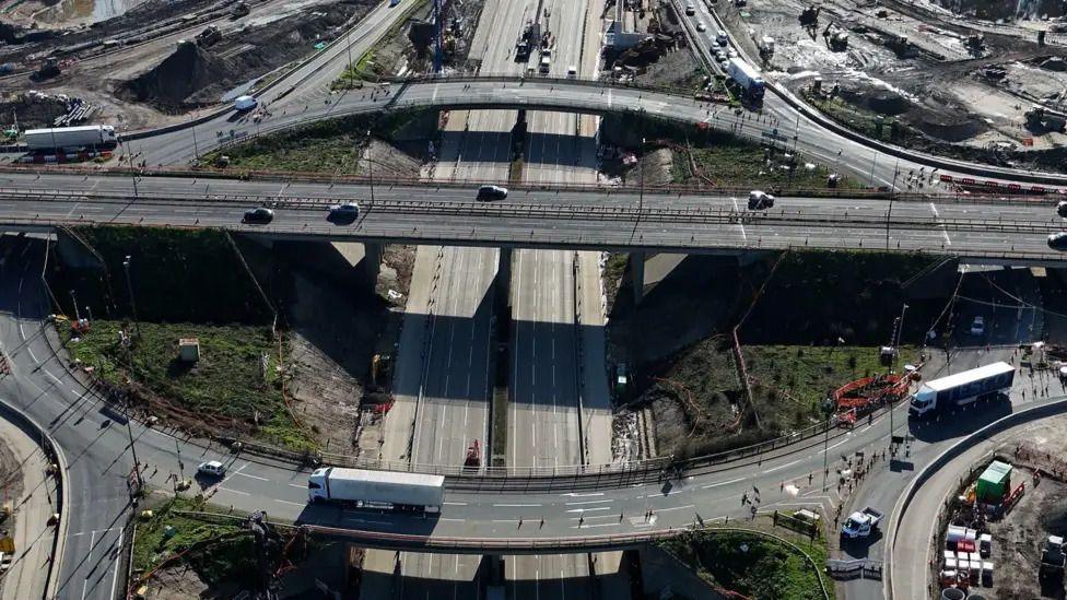 Junction 10 of the M25 seen from above. There are a number of vehicles driving on the roads, and an area of grass in the middle.