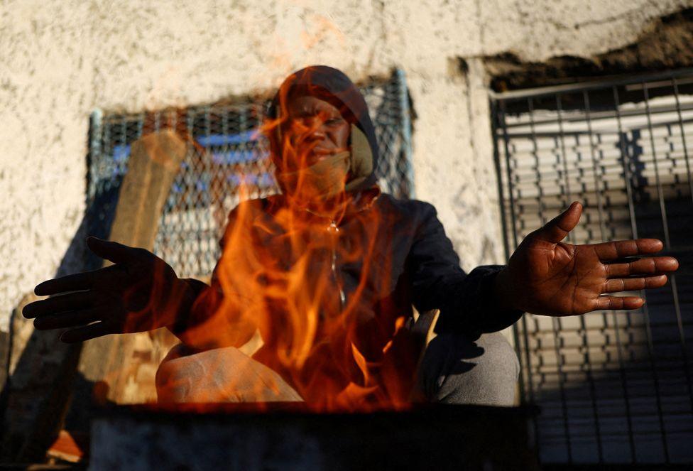 Dumisani Cele holds his hands up as he warms himself with a brazier in Johannesburg