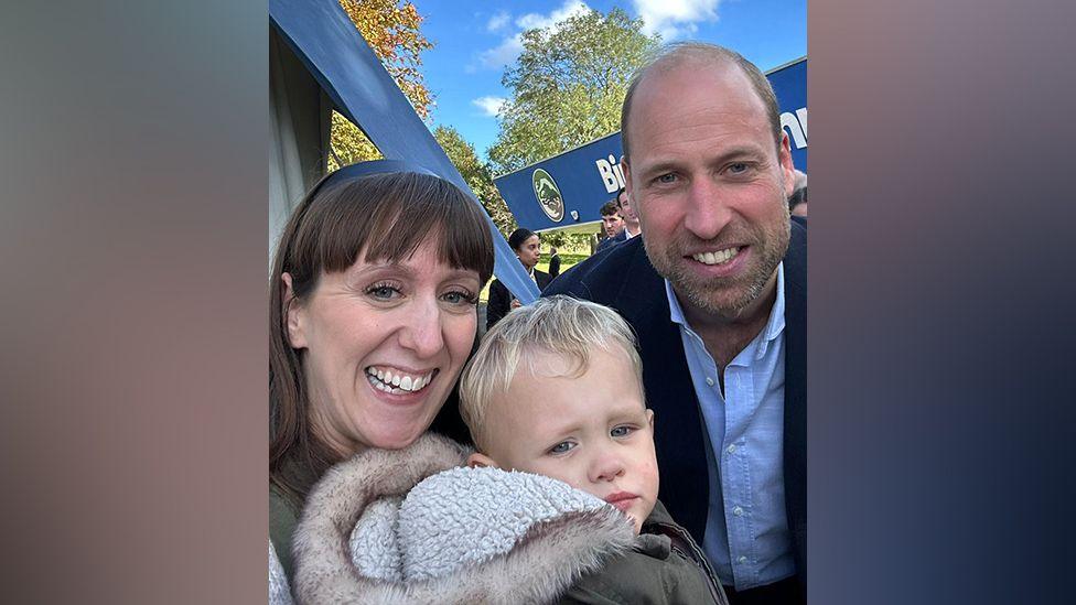 Rachel Arnott and one of her three children, wearing a coat with a furry hood, with Prince William outside Birtley Community Pool.