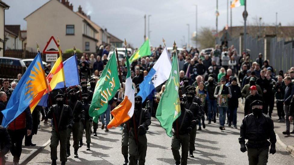 Masked men in combat uniforms take part in the dissident parade through the Creggan estate in Derry in April 2023