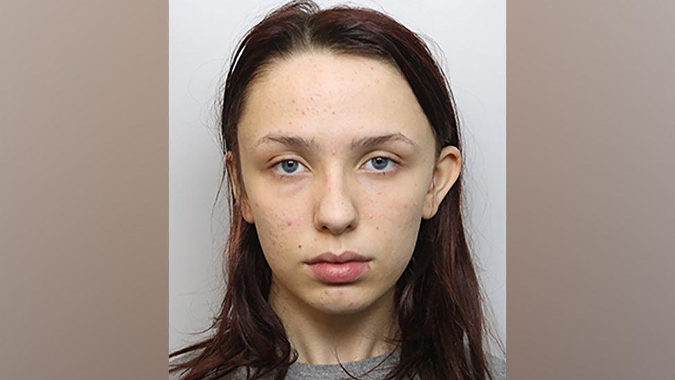 Scarlett Jenkinson, with long brown hair and wearing a grey sweatshirt, stares at the camera