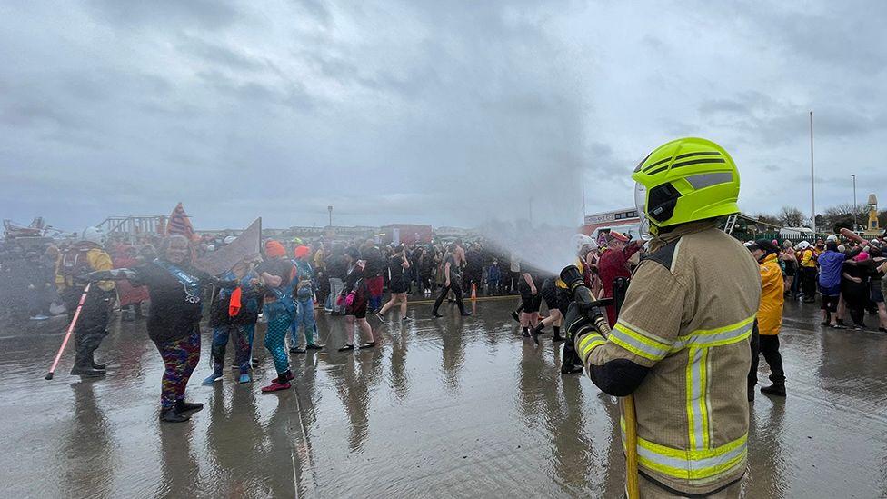 A firefighter sprays the crowd of swimmers with water form the fire engine's hosepipe