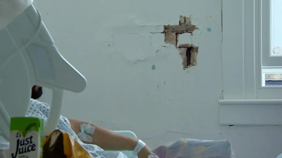 Large holes in the brick wall along the side of a ward. A patient can be seen laying nearby