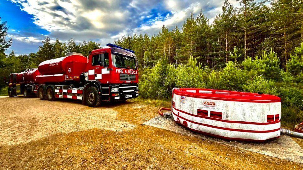 Fire service water carrier to left of inflatable white with red striped water reservoir - similar to round a garden pool