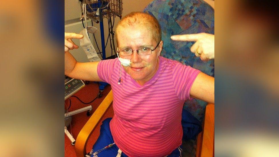 Jo Burridge sat in a hospital chair receiving treatment pointing at her head.