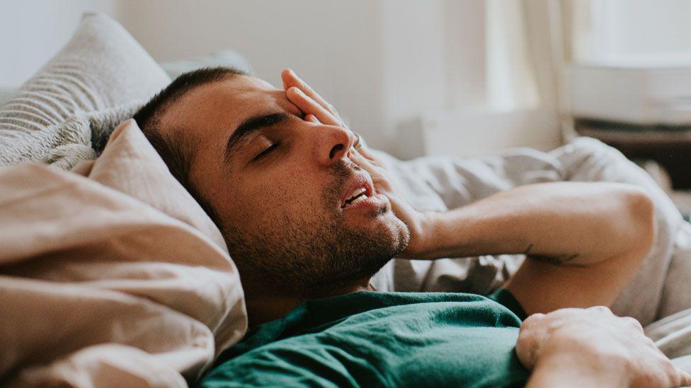 Man looking unwell and holding his head in bed