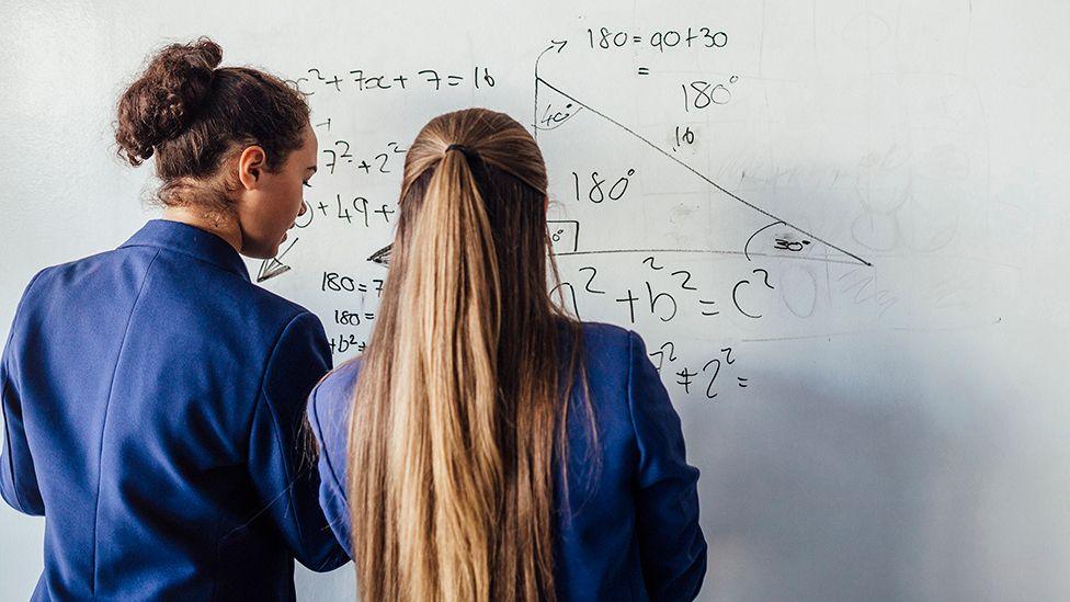 The backs of two female students in front of a white board doing maths