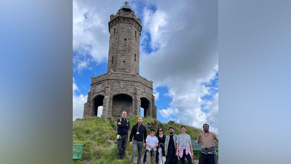 A group of people standing at the foot of Jubilee Tower on Darwen Moor on a sunny day