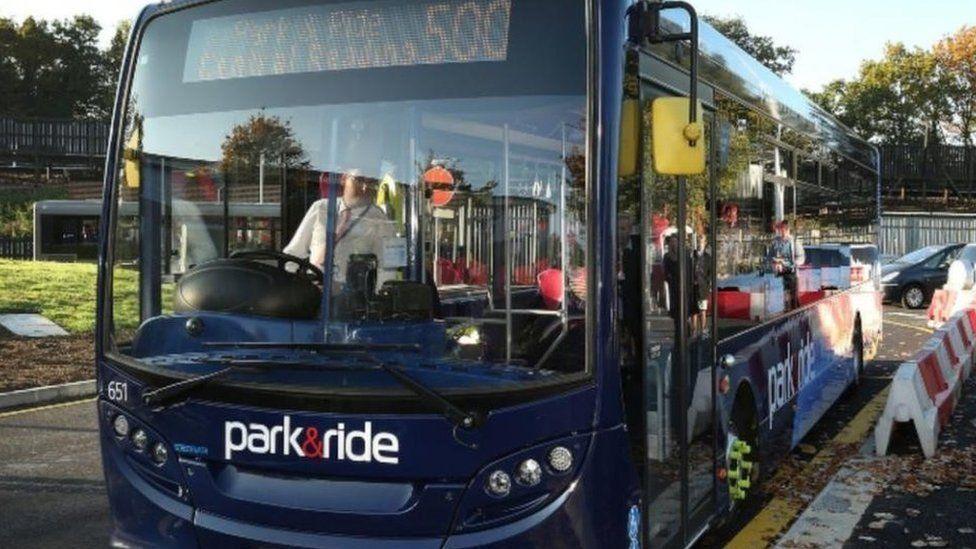 Navy blue single decker park and ride bus pulled in with doors shut and driver white white shirt