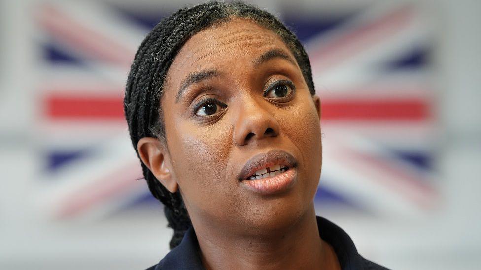 Kemi Badenoch speaking, with a blurred Union Jack in the background