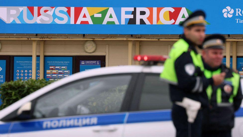 Two traffic police officers near a police car stand guard on a roadside with branding for the Russia-Africa summit seen behind them in Sochi, Russia - 8 November 2024