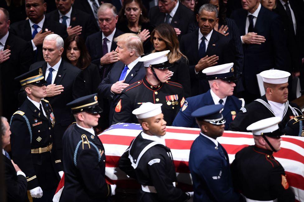 Coffin carrying George HW Bush is carried past Mike Pence, Donald Trump, Melania Trump and Barack Obama as they each hold their right hand against their chest as a mark of respect