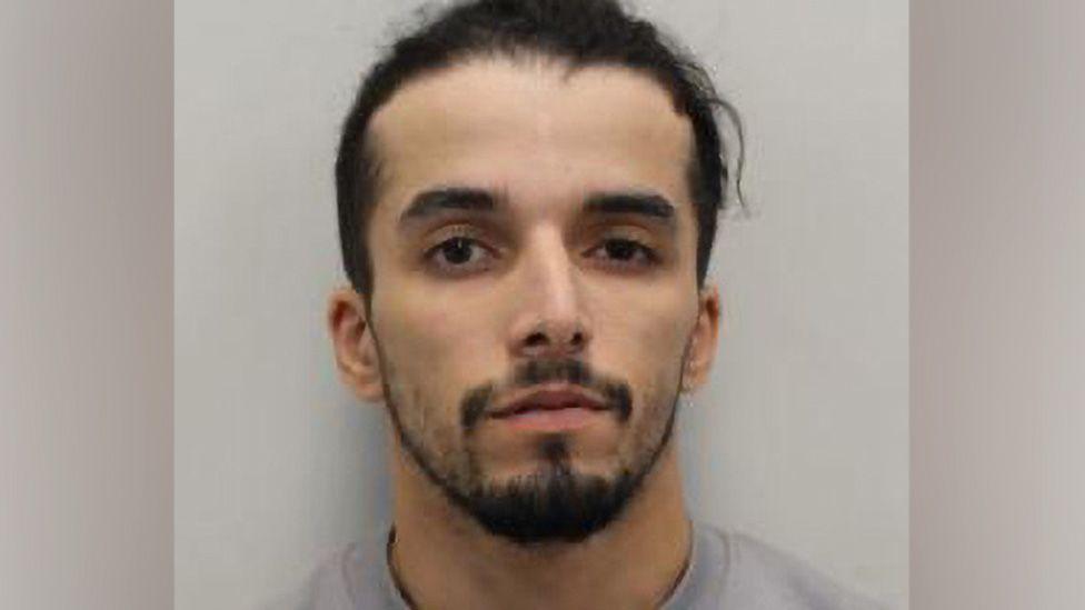 Brahim Kaddour-Cherif mugshot. He is looking at the camera. He has dark hair and a beard and is wearing a grey jumper