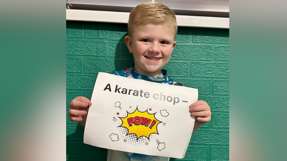 Stanley holding a white sign with black writing saying 'a karate chop'. Below it is a red comic book style 'pow'.