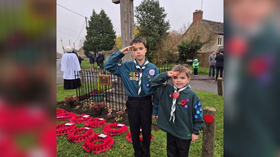 Nathan and Oscar Lee on Parade in Stonesfield, Oxfordshire wearing their scouts uniform and holding a salute.