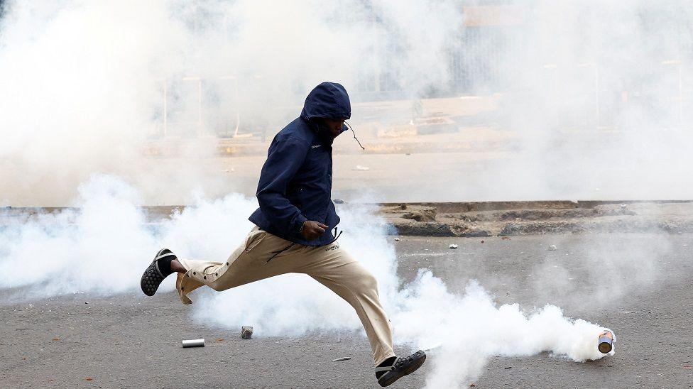 A man shields his face and runs away from a tear gas canister.