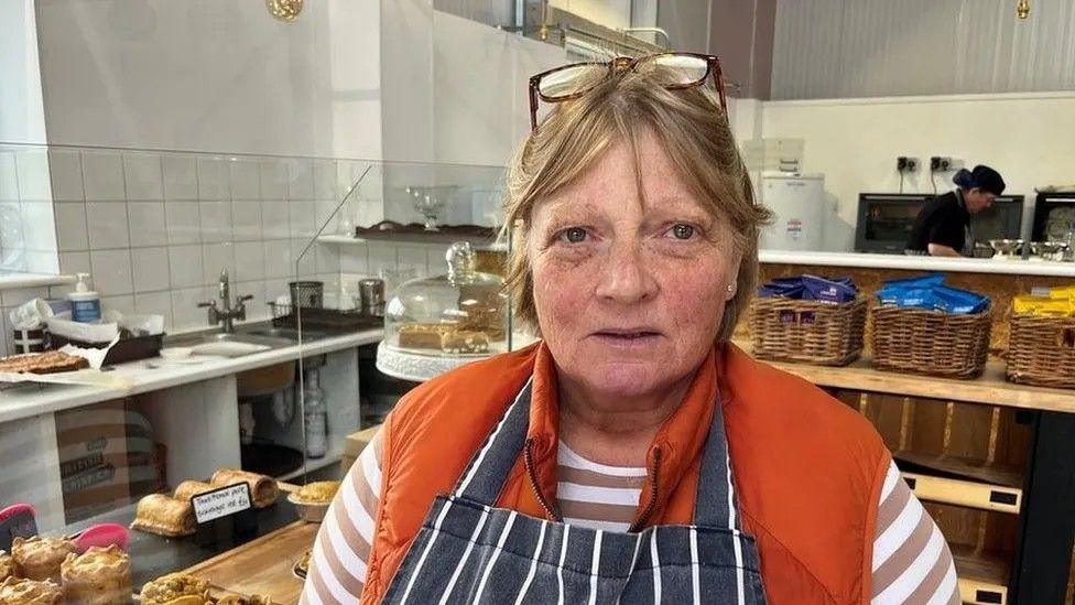 Penny Williams with glasses on her head, wearing a baker's pinny, in a bakery