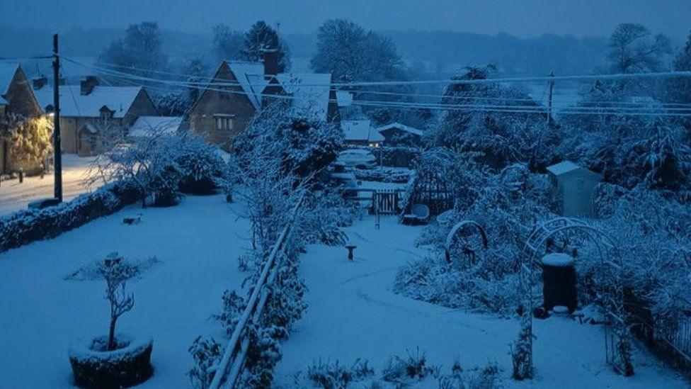 Snow covered gardens leading up to homes - it's just getting light.