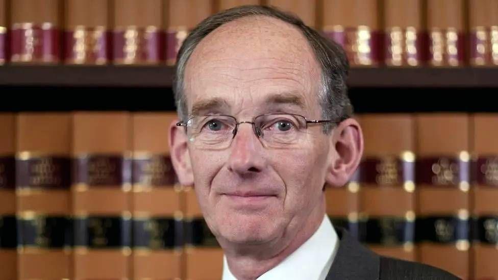 Sir Andrew McFarlane head-and-shoulders shot, with him standinf in front of shelves of legal tomes