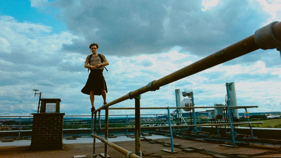 Film still from Bird showing Franz Rogowski standing on a metal fence