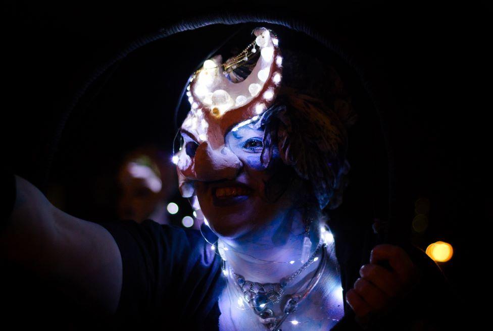 A woman wearing facial prosthetics as part of a costume, lit up with small lights. 