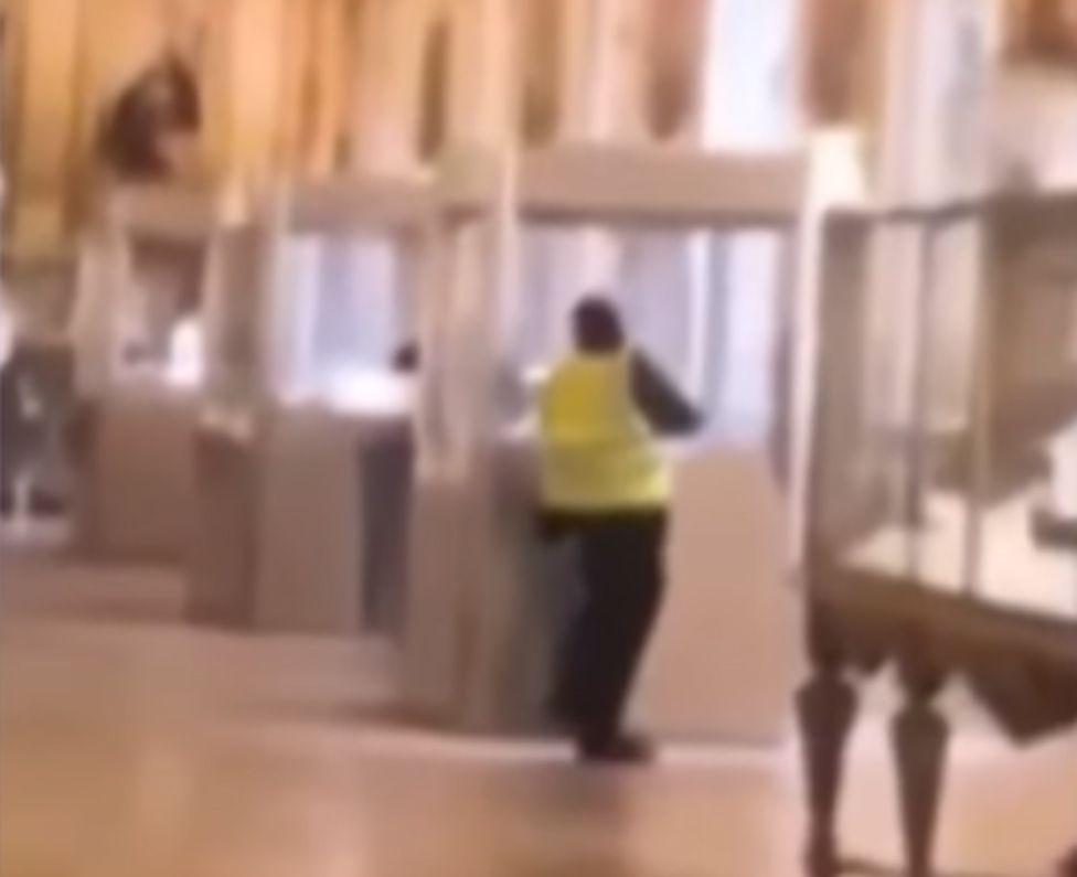 A robber smashes a glass case in the Louvre.