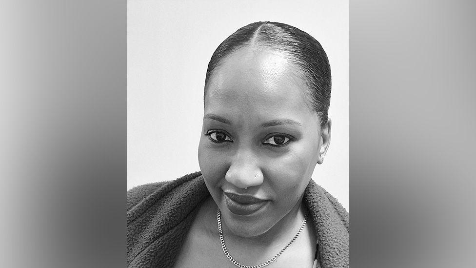 A black and white selfie of a woman with her hair in a bun and wearing a chain necklace