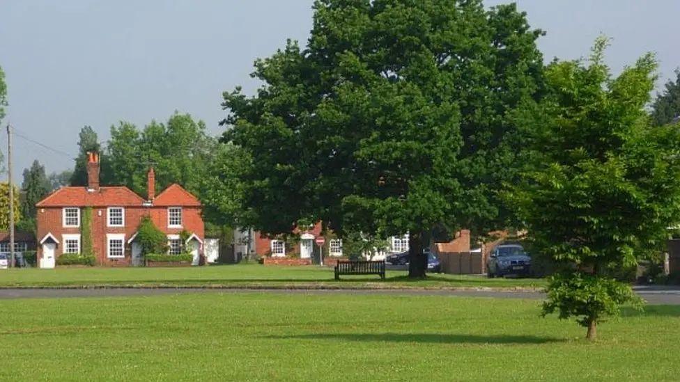 View of Holyport with an area of grass and trees in front of red-brick semi-detached houses