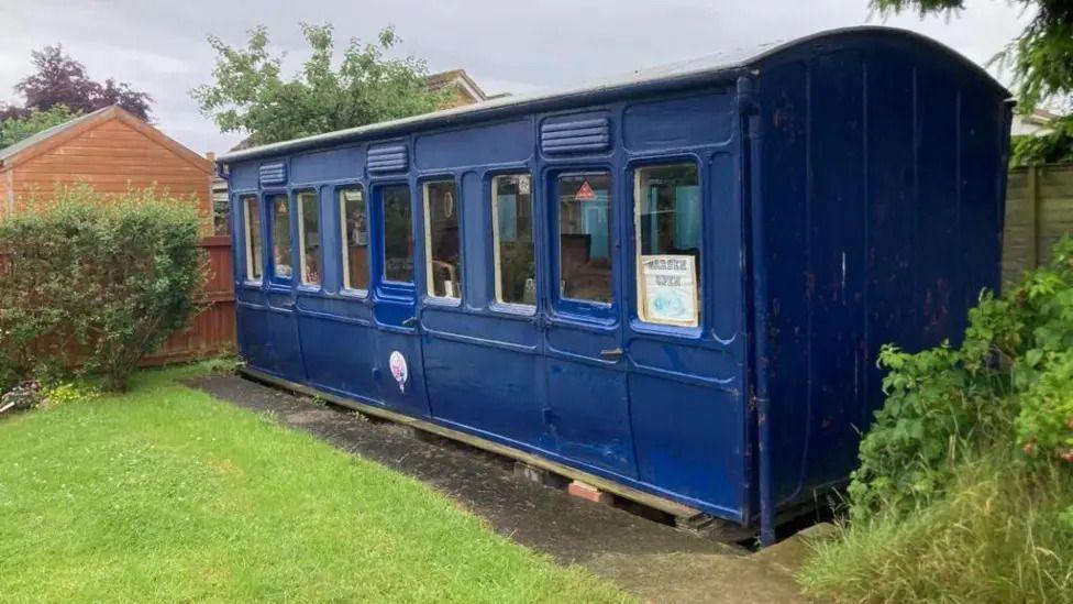 An old railway carriage painted blue. It is in a private garden.