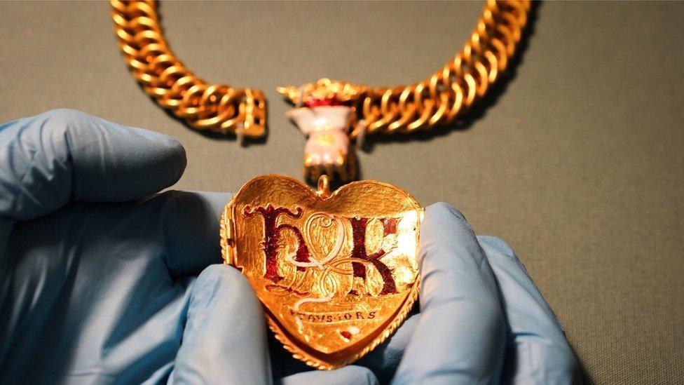 The back of a gold pendant with the letters H and K in red