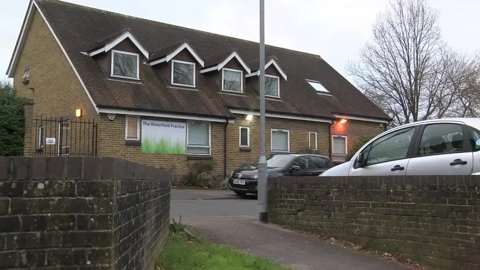 A general view of the Waterfield Practice in Bracknell, a two storey building with a sign saying "The Waterfield Practice" and two cars parked in its car park