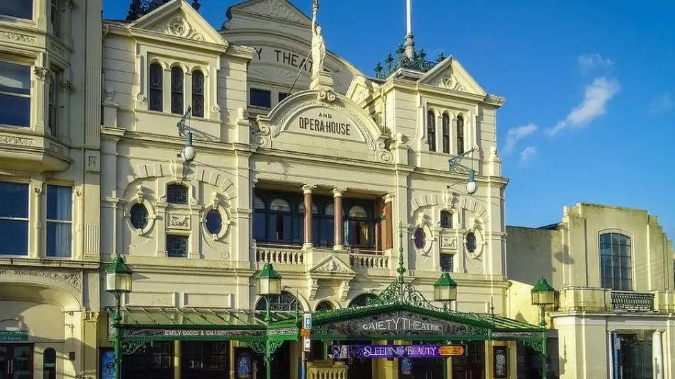 The outside of the Gaiety Theatre, a Victorian style grand cream coloured building with a balcony with two columns and a dark green shelter that reads Gaiety Theatre.