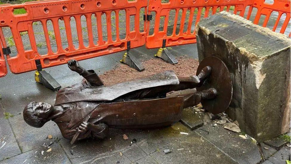 The Victoria Wood statue in Bury, knocked over on the ground and covered in debris.