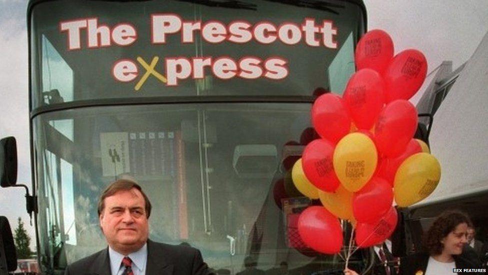 John Prescott stands in front of a bus with a sign saying The Prescott Express 