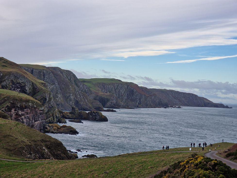 The rugged Berwickshire coastline and seaside on a cloudy day with a few visitors like tiny specks in the foreground