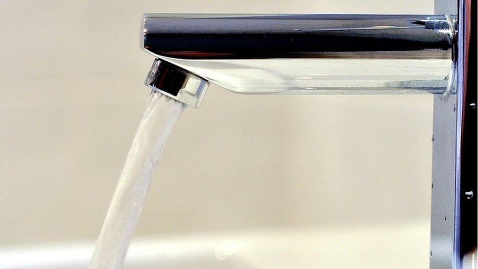 An open stainless steel tap with water rushing out of the spout and a white background